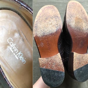 May include: A pair of brown leather shoes with a crocodile pattern. The shoes have a black rubber sole and the text "Calvin Klein" is printed on the inside of the shoe.