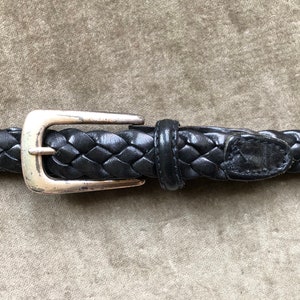 Puede incluir: Un cinturón de cuero trenzado negro con una hebilla plateada.