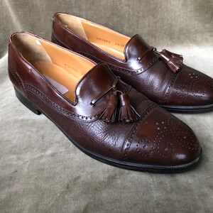 May include: A pair of brown leather tassel loafers with a wingtip design and a perforated pattern. The loafers have a brown leather tassel on each shoe.