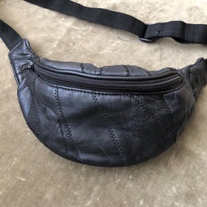 May include: Black leather fanny pack with a zippered main compartment and adjustable black strap. The pack features a quilted design with visible stitching. A classic and practical accessory.