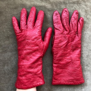 Puede incluir: Un par de guantes de cuero rojo. Los guantes están hechos de cuero texturizado y tienen un estilo clásico.