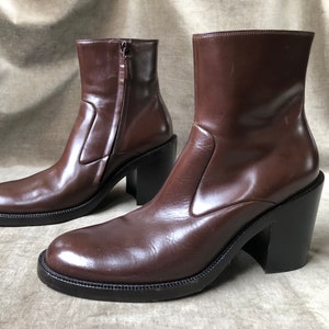 May include: A pair of brown leather ankle boots with a chunky heel. The boots have a pointed toe and a zipper on the inside of the ankle.