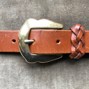 May include: A brown leather belt with a gold metal buckle and a braided leather keeper.