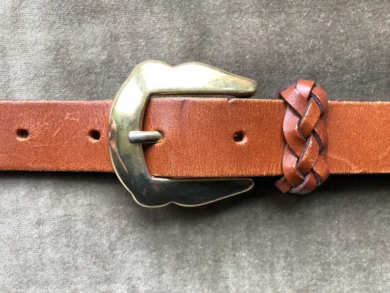 May include: A brown leather belt with a gold metal buckle and a braided leather keeper.