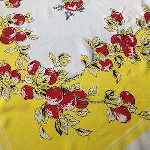 May include: A vintage white tablecloth with a yellow border and a repeating pattern of red apples and green leaves on branches. The apples have white highlights, and the leaves are outlined in black.