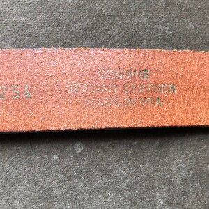 May include: Close-up of a brown leather belt with the text "Genuine Leather Made in USA" and the size "125" printed on it.