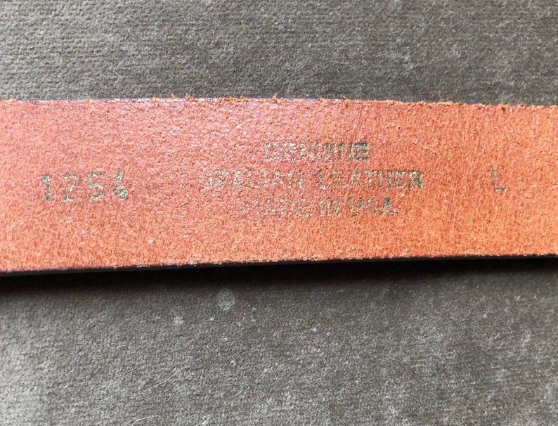 May include: Close-up of a brown leather belt with the text "Genuine Leather Made in USA" and the size "125" printed on it.