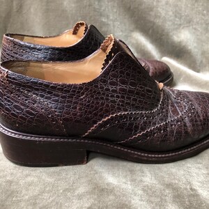 May include: A pair of brown leather brogue shoes with a textured finish. The shoes have a lace-up closure and a rounded toe.
