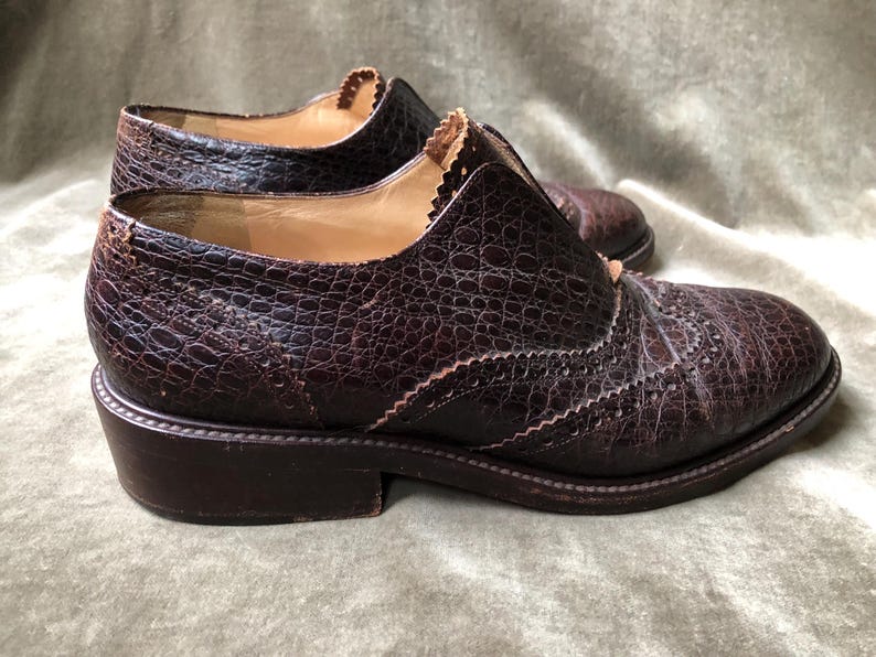 May include: A pair of brown leather brogue shoes with a textured finish. The shoes have a lace-up closure and a rounded toe.