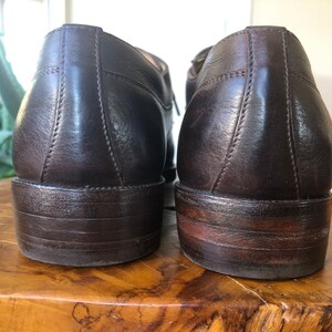 Puede incluir: Un par de zapatos marrones de cuero con cordones y un acabado ligeramente desgastado. Los zapatos tienen una punta redonda y un tac&oacute;n bajo.