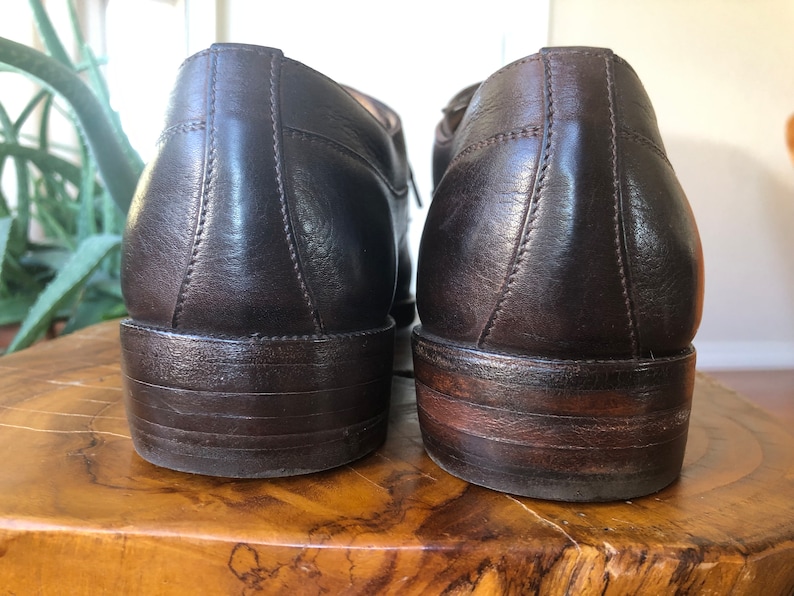 Puede incluir: Un par de zapatos marrones de cuero con cordones y un acabado ligeramente desgastado. Los zapatos tienen una punta redonda y un tac&oacute;n bajo.