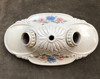 Peut inclure: Plafonnier de plafond de style vintage blanc cassé avec deux douilles. Le luminaire présente un motif floral avec des fleurs peintes en rose et bleu. Le motif central est une grande fleur stylisée. Le luminaire est en céramique ou en porcelaine.