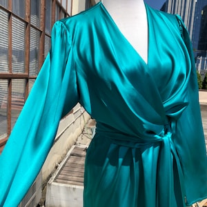 Könnte beinhalten: Ein blaues Satin-Wickelkleid mit langen Ärmeln und V-Ausschnitt. Das Kleid hat einen Gürtel an der Taille.