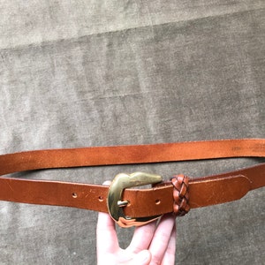 May include: A brown leather belt with a gold buckle and a braided leather strap.