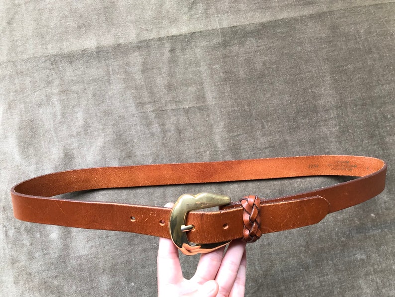 May include: A brown leather belt with a gold buckle and a braided leather strap.