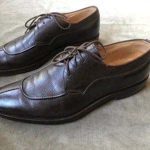 Puede incluir: Un par de zapatos marrones de cuero con cordones, punta puntiaguda y tac&oacute;n ligeramente elevado.