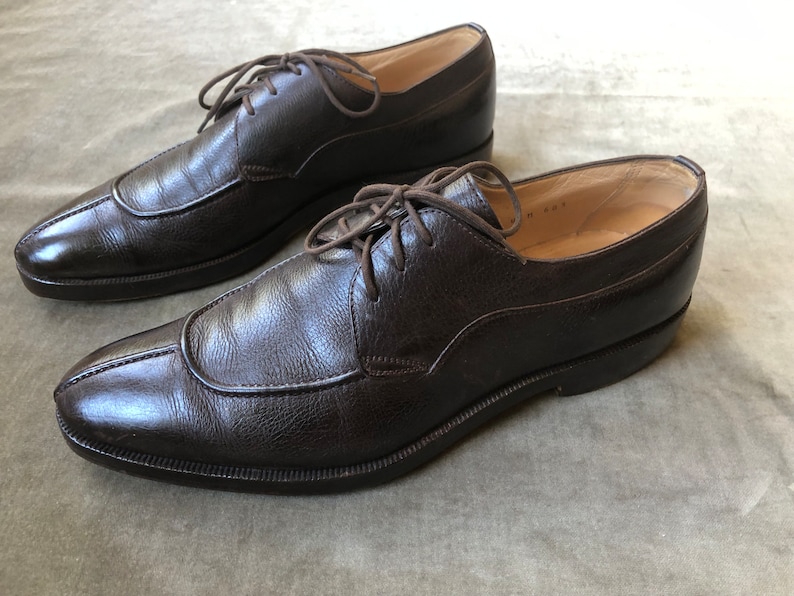 Puede incluir: Un par de zapatos marrones de cuero con cordones, punta puntiaguda y tac&oacute;n ligeramente elevado.