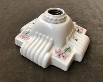 Peut inclure: Base de luminaire en céramique blanc cassé avec un motif floral. La base est carrée avec des bords arrondis et des détails côtelés verticaux. Des fleurs roses avec des feuilles vertes sont peintes à la main sur les coins.