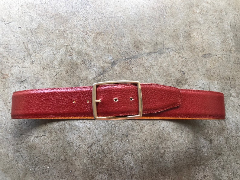May include: A red leather belt with a gold metal buckle.
