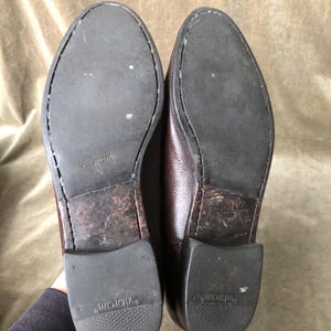 May include: A pair of brown leather shoes with a worn leather sole. The soles are marked with the word "Vibram" and the size 8.