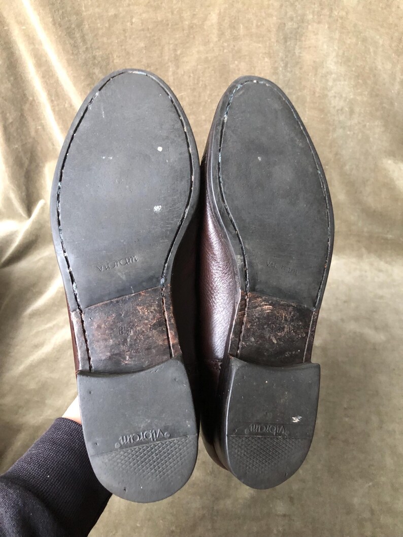 May include: A pair of brown leather shoes with a worn leather sole. The soles are marked with the word "Vibram" and the size 8.