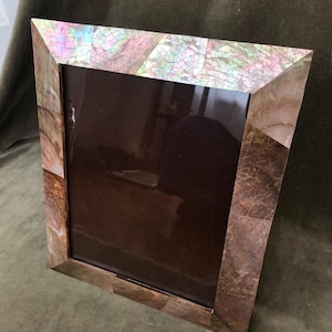 May include: A rectangular picture frame featuring a mosaic border composed of iridescent shell fragments. The top section displays light, pearlescent pink and green tones, while the side and bottom sections transition into deeper, earthy brown and copper hues.
