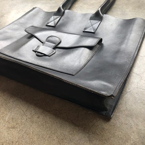 Puede incluir: Un bolso tote de cuero negro con un bolsillo frontal grande y dos asas superiores.