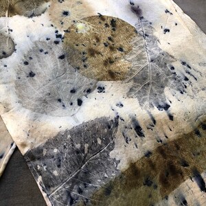 May include: A white silk scarf with a leaf pattern in shades of brown, gray, and blue. The leaves are arranged in a random pattern and have a natural, organic look.