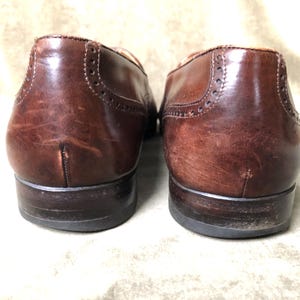 May include: A pair of brown leather brogue shoes with a wingtip design. The shoes have a polished finish and are in good condition.
