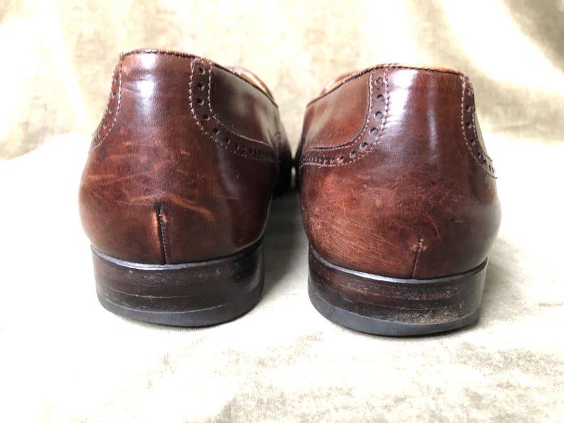 May include: A pair of brown leather brogue shoes with a wingtip design. The shoes have a polished finish and are in good condition.