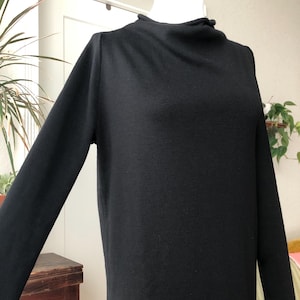 May include: A black long-sleeve dress with a mock turtleneck. The dress is made of a soft, knit fabric and has a simple, elegant design. The dress is displayed on a mannequin.
