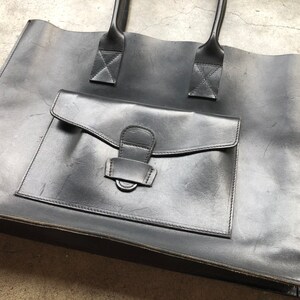 Puede incluir: Un bolso tote de cuero negro con un bolsillo frontal grande y dos asas superiores.