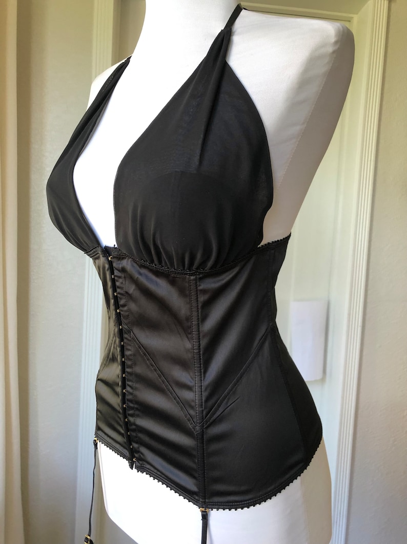 Pode incluir: Corpete de cetim preto com decote halter e ferragens douradas. O corpete tem uma estrutura com varas e uma borda de renda.