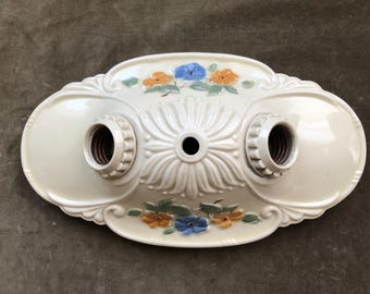 Peut inclure: Plafonnier ovale crème avec deux douilles. Le luminaire présente un motif floral avec des accents peints en orange, bleu et vert. Le centre a un motif en forme de fleur.