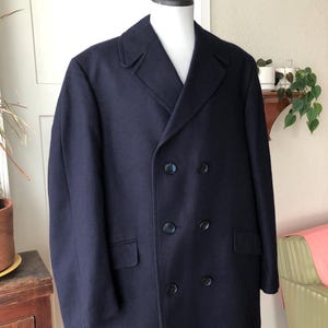 Peut inclure: Un pardessus bleu marine à double boutonnage avec un col cranté et deux rangées de boutons. Le manteau a deux poches avant et est présenté sur un mannequin. Le manteau est de style classique.