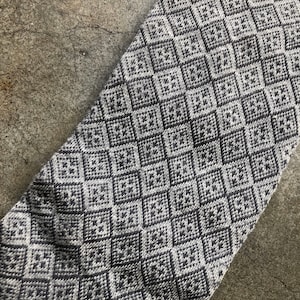 May include: A close-up of a gray and white patterned fabric with a diamond pattern. The fabric is soft and textured.