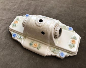 Peut inclure: Luminaire en céramique blanc cassé avec une texture tressée sur le cylindre central. La base rectangulaire est ornée de motifs floraux bleus, oranges et verts. Il comporte deux trous et une douille.