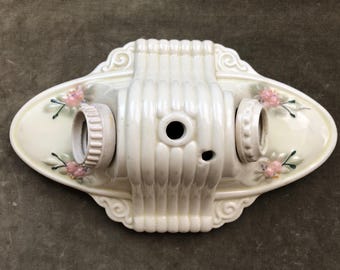 Peut inclure: Luminaire en céramique blanc cassé avec deux douilles et des motifs floraux. Le luminaire est de forme ovale avec un motif central nervuré et des bords décoratifs. Des fleurs roses et des feuilles vertes sont peintes sur les côtés.