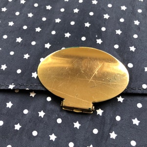 May include: A gold-colored oval-shaped clasp with a small latch on a black fabric background with white stars and dots.