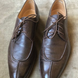 Puede incluir: Un par de zapatos marrones de cuero con cordones, punta puntiaguda y una costura decorativa en la parte delantera.