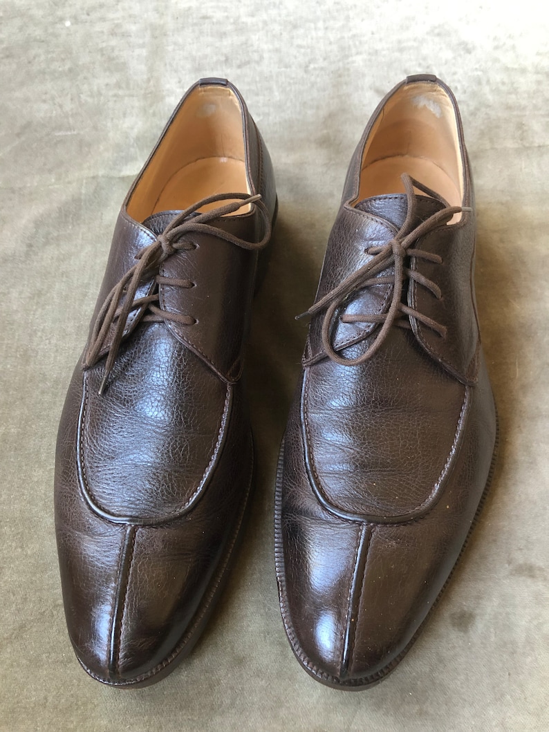 Puede incluir: Un par de zapatos marrones de cuero con cordones, punta puntiaguda y una costura decorativa en la parte delantera.