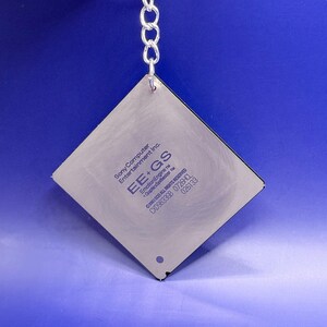 Puede incluir: Un llavero de metal de forma cuadrada que presenta un chip de procesador de computadora de tono plateado. La superficie está grabada con el texto Sony Computer Entertainment Inc. EE+GS EmotionEngine GraphicsSynthesizer 2001 SCEI ALL RIGHTS RESERVED CXD9833GB 0726HCL 026133.