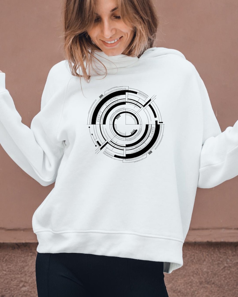 May include: White hoodie featuring a black and white circular geometric design on the front. The design consists of concentric circles, lines, and rectangular shapes. The hoodie has a drawstring hood and long sleeves.