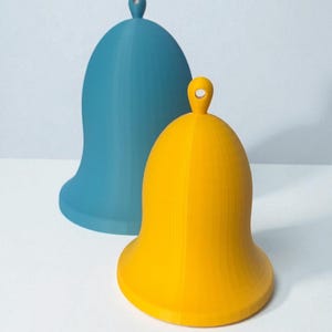 May include: Two bell-shaped objects, one teal and one yellow, are displayed against a white background. Each bell has a rounded top with a small loop. The bells have a smooth, matte finish and a wide base.
