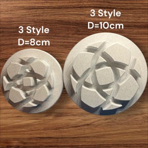 Puede incluir: Dos objetos circulares de color gris claro con un diseño geométrico. El más grande tiene 10 cm de diámetro y el más pequeño 8 cm. El texto "3 Style" está encima de cada objeto. Los objetos están sobre una superficie de madera.
