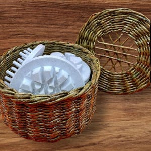 May include: A wicker basket with a lid, holding white, geometric items. The basket is made of brown and orange woven material. The lid is also woven, with a circular pattern.