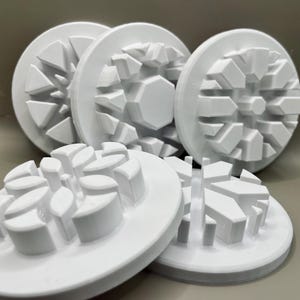 May include: Several white, circular objects with geometric, raised patterns. The objects are arranged in a group, with some overlapping. The designs include triangular and hexagonal shapes, creating a textured surface. The items appear to be made of a solid, durable material.