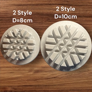 Könnte beinhalten: Zwei kreisförmige, cremefarbene, strukturierte Stempel mit geometrischen Designs. Der kleinere Stempel hat einen Durchmesser von 8 cm, der größere 10 cm. Der Text "2 Style" steht über jedem Stempel. Auf einer Holzoberfläche.