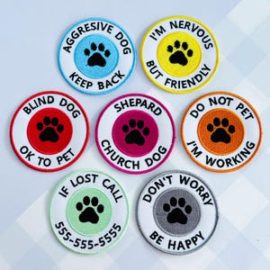 May include: A collection of round embroidered patches with various messages and paw print designs. Colors include blue, yellow, red, pink, orange, green, and gray. Text includes "Aggressive Dog," "Blind Dog," "Nervous," and "Do Not Pet."