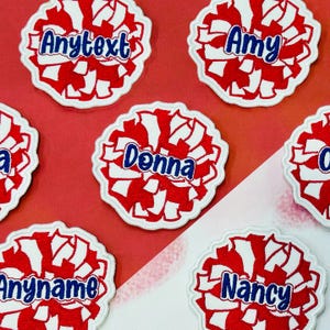 May include: Red and white pom-pom shaped patches with embroidered names in blue. The patches have a white border and are arranged on a red and white background. Names include "Amy", "Donna", "Nancy", and "Anyname".